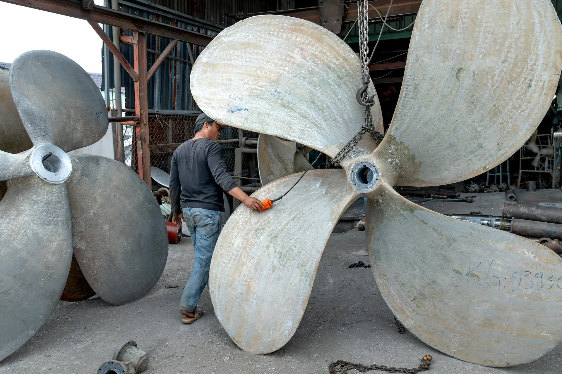 Workers performing maintenance on large ship propellers in a marine repair workshop